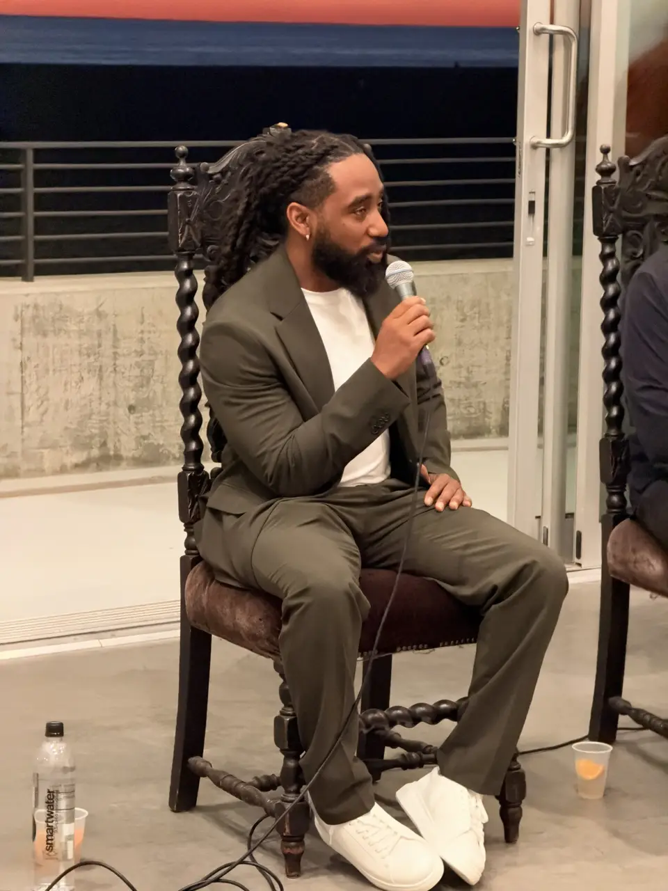 Movement BE founder Nate Howard, in an olive suit, speaks into a microphone while seated on stage.