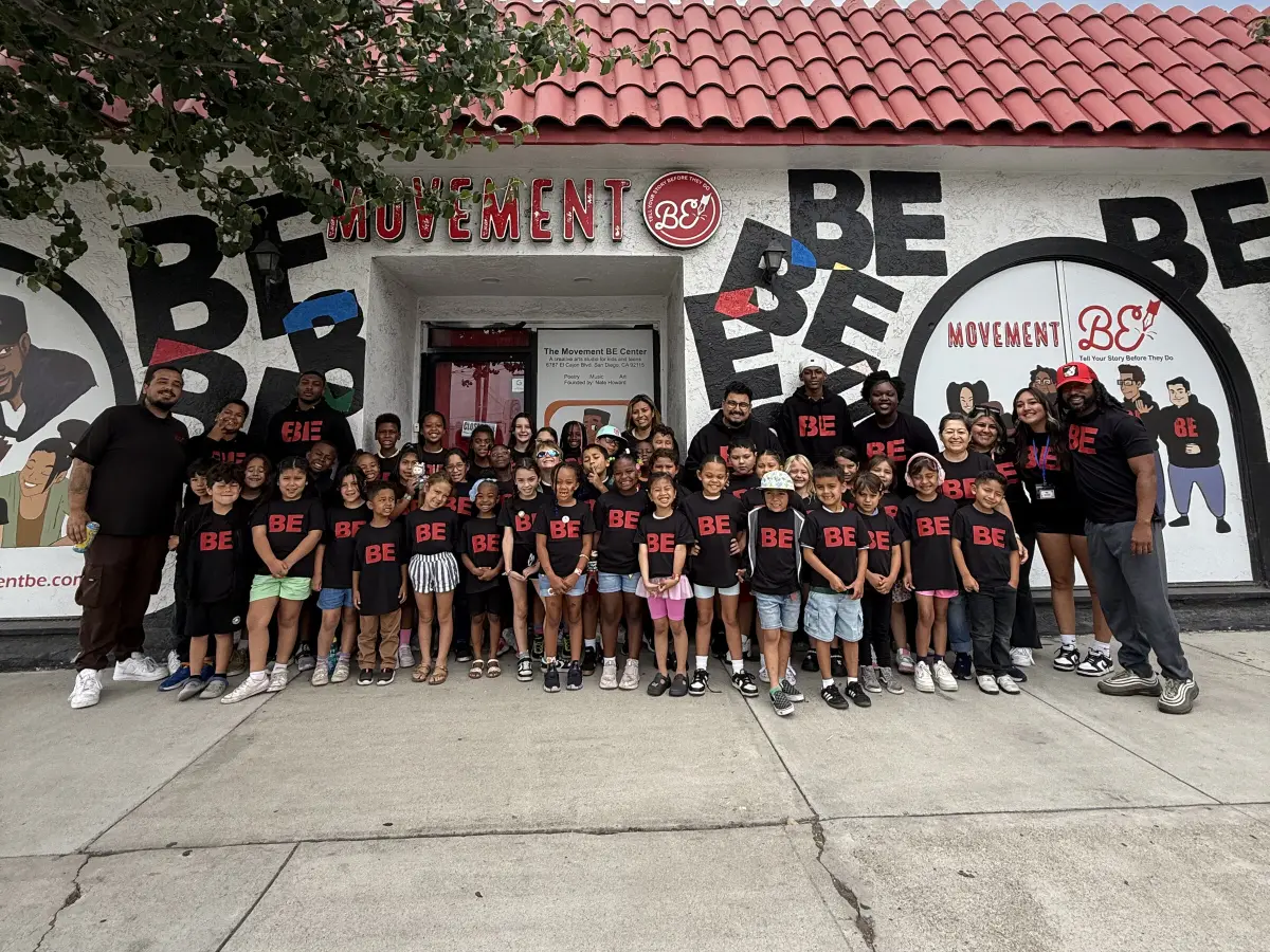 Dozens of children in matching black BE T-shirts stand with staff in front of the Movement BE center.